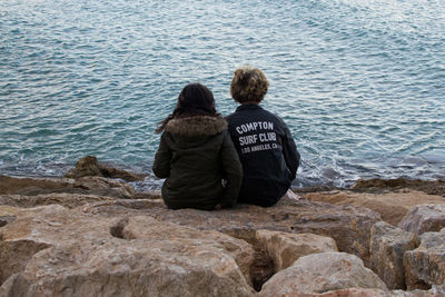 Rear view of woman sitting on rock by sea