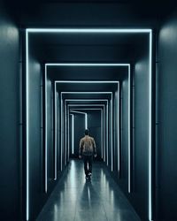 Rear view of man walking in illuminated corridor