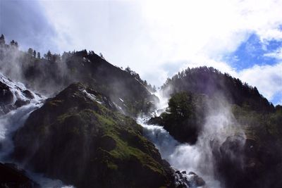 Low angle view of waterfall in forest against sky