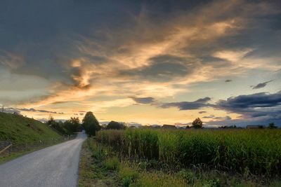 Road amidst field against sky during sunset