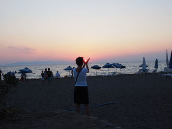 Women standing on beach against sky during sunset