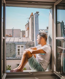 Side view of man sitting on window