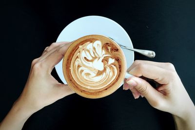 Cropped image of woman hand holding fresh coffee cup on table at cafe