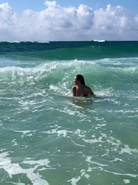 Smiling young woman swimming in sea against sky