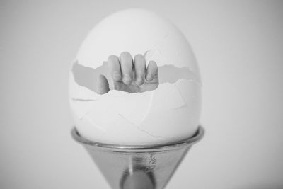 Digital composite image of hand breaking eggshell against white background