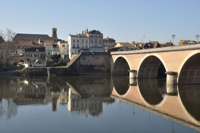 Arch bridge over river by buildings against clear sky