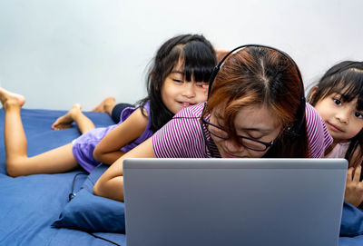 Cute girls and mother looking at laptop while lying on bed