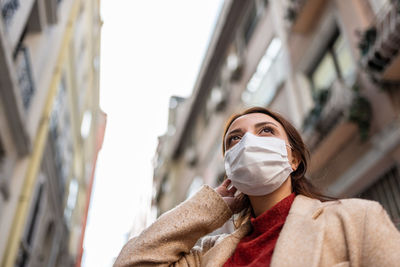 Low angle view of woman wearing mask standing against sky