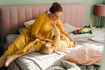 Mom tickles and hugs her little daughter in the morning on the bed in the apartment.