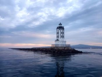 Lighthouse on sea by building against sky