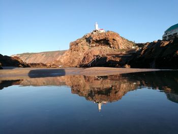 Reflection of lighthouse in water against clear blue sky