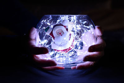 Close-up of hand holding illuminated lighting equipment against black background