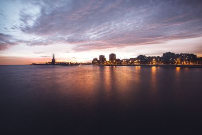 Scenic view of river by buildings against sky during sunset