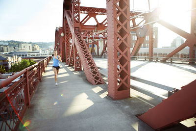 Female athlete running on footbridge in city during sunny day