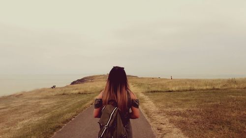 Rear view of woman with backpack standing on road against sky