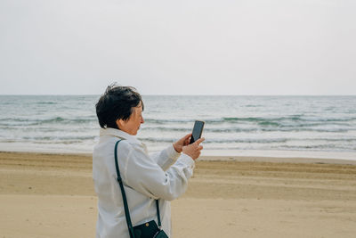 An adult woman on the beach near the ocean in the spring at a picnic takes a selfie, talks a video