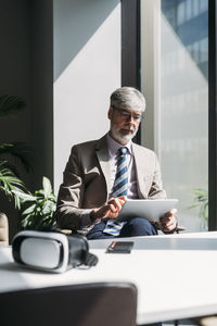 Businessman using tablet pc sitting by window in office