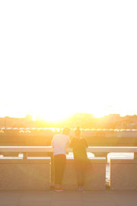 Rear view of young couple standing on bridge during sunset