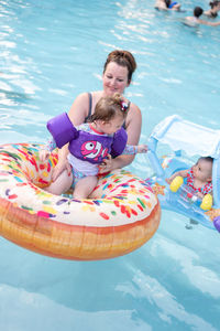 Mother holding daughters sitting on inflatable ring in swimming pool