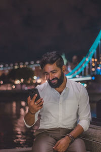 Man using mobile phone while sitting against sky at night