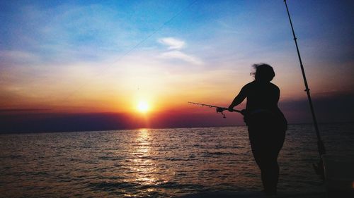 Silhouette woman fishing in sea against sky during sunset