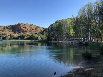 Scenic view of lake by trees against clear blue sky