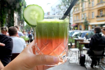 View of person holding glass of tropical juice while other people at outdoor caf