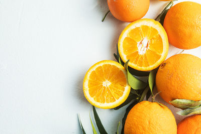 Flat lay of citrus fruits like lime, orange and lemon with leaves on light colored background.