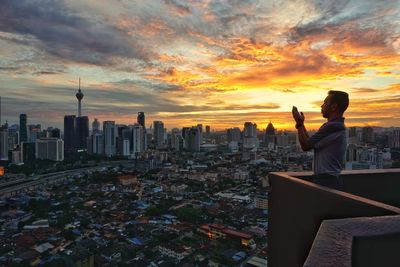 Man photographing cityscape against cloudy sky during sunset
