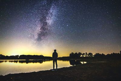 Rear view of silhouette standing on lake at night