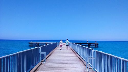 Rear view of people standing on pier at sea against clear sky