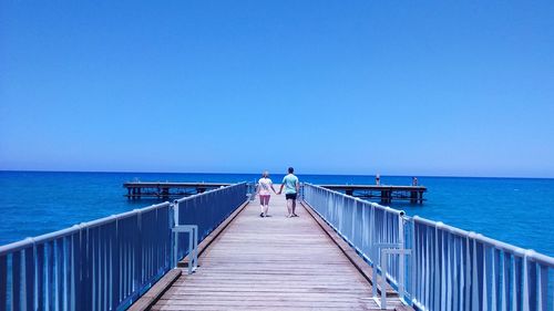 Rear view of people walking on pier at sea against clear sky