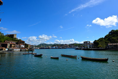 Boats moored at harbor by buildings against blue sky