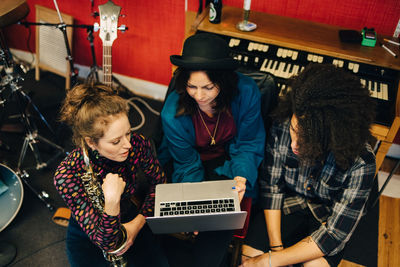 Male and female friends with various instruments looking at laptop at recording studio
