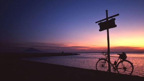 Bicycle at beach against sky during sunset
