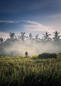 Rear view of woman walking on field against sky during sunset