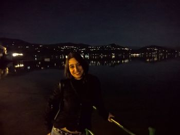 Portrait of smiling woman standing against illuminated city at night