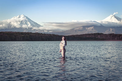 Side view of young woman looking away while standing in lake against sky during sunset
