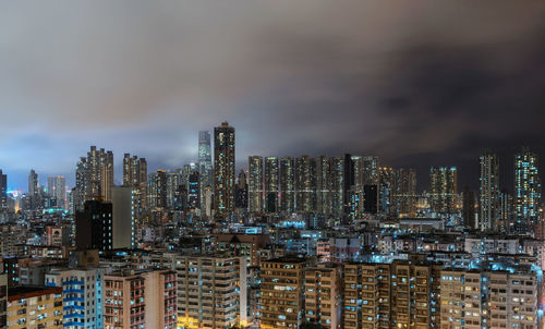Aerial view of illuminated modern buildings in city against cloudy sky