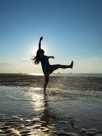 Happy silhouette woman splashing water on shore at beach during sunset