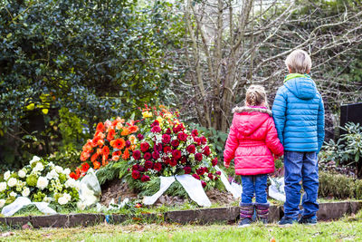 Siblings standing against flowers in graveyard