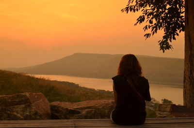 Rear view of woman standing on mountain against sunset sky