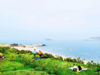 People on grassy field against sea and sky