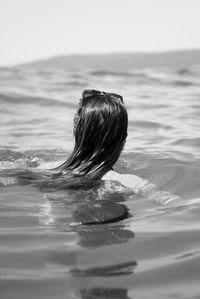 Rear view of woman swimming in sea against clear sky