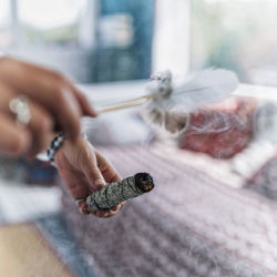 Cropped image of sage holding feather with smudge stick indoors