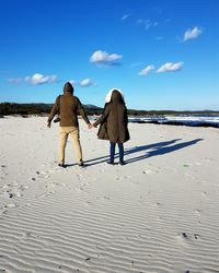 Rear view of people walking on beach against sky