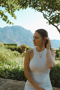 Side view of young woman standing on field against sky