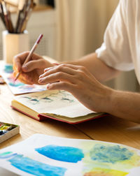 The artist's hands with a brush. an artist's sketchbook lying on the desktop. the workflow 