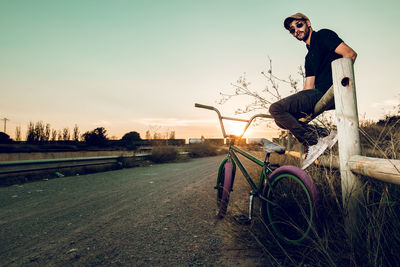 Side view portrait of man sitting with bicycle on road during sunset