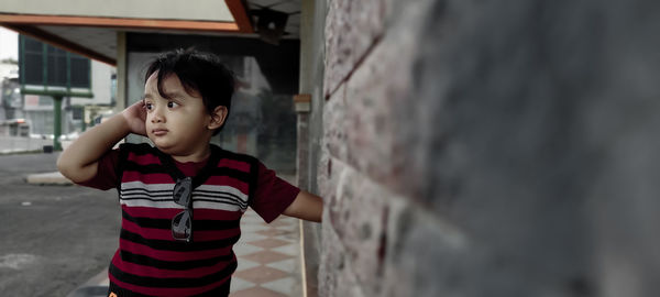 Boy looking away while standing against wall